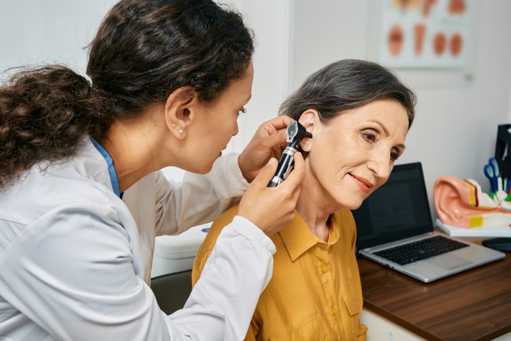 Audiological assessment for elderly citizen people. Otolaryngologist doctor checking mature woman's ear using otoscope or auriscope at medical clinic