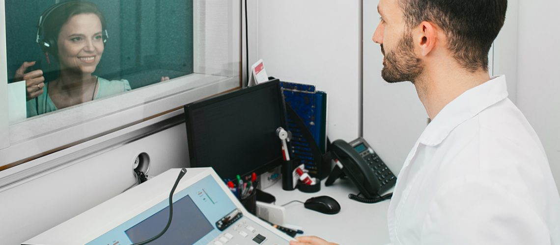 Audiometric technician doing the hearing test on an adult woman using an audiometer in a mobile audio room.